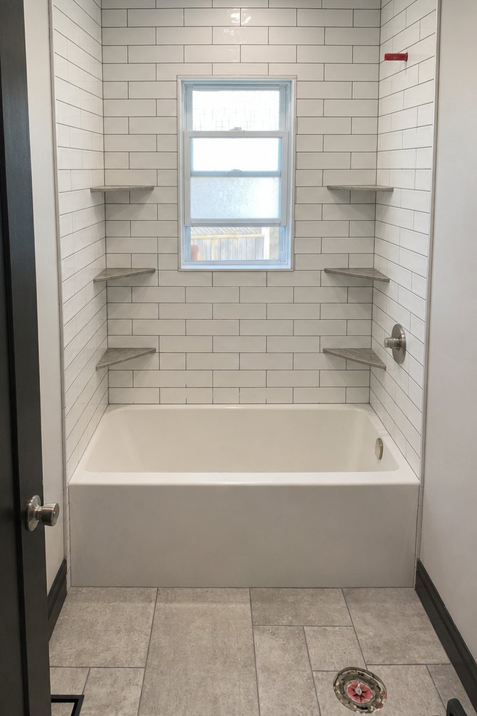 Finished bathroom with white subway-tile tub surround, tiled floor and built-in shelving by MacNeil Home Solutions